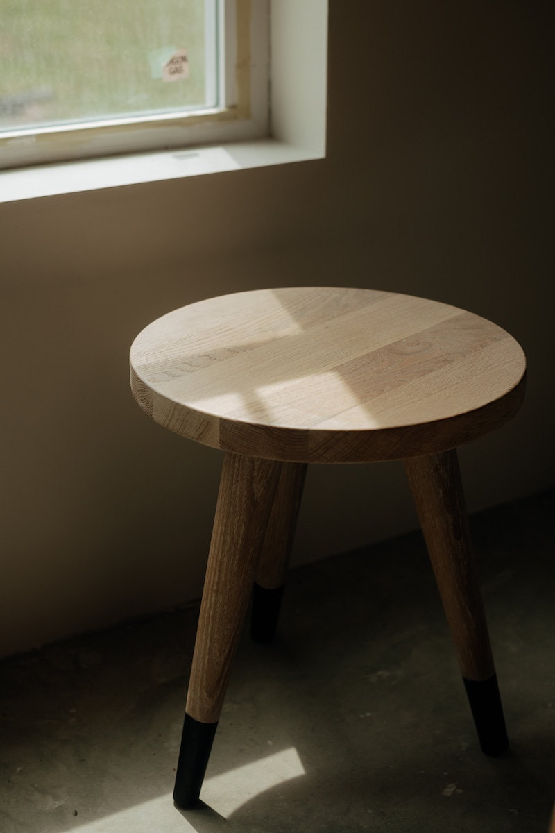 A round, wooden side table, made by Crafted Glory, bathed in light streaming through a nearby window