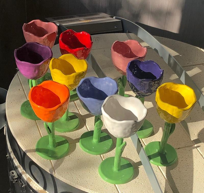 Nine handmade tulip-shaped ceramic goblets in different colors.