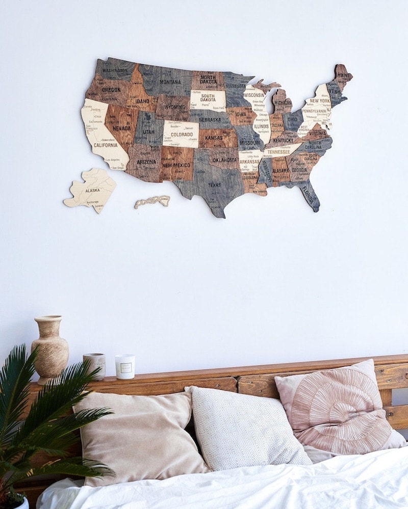 A wooden travel map hanging on the wall above a bed.