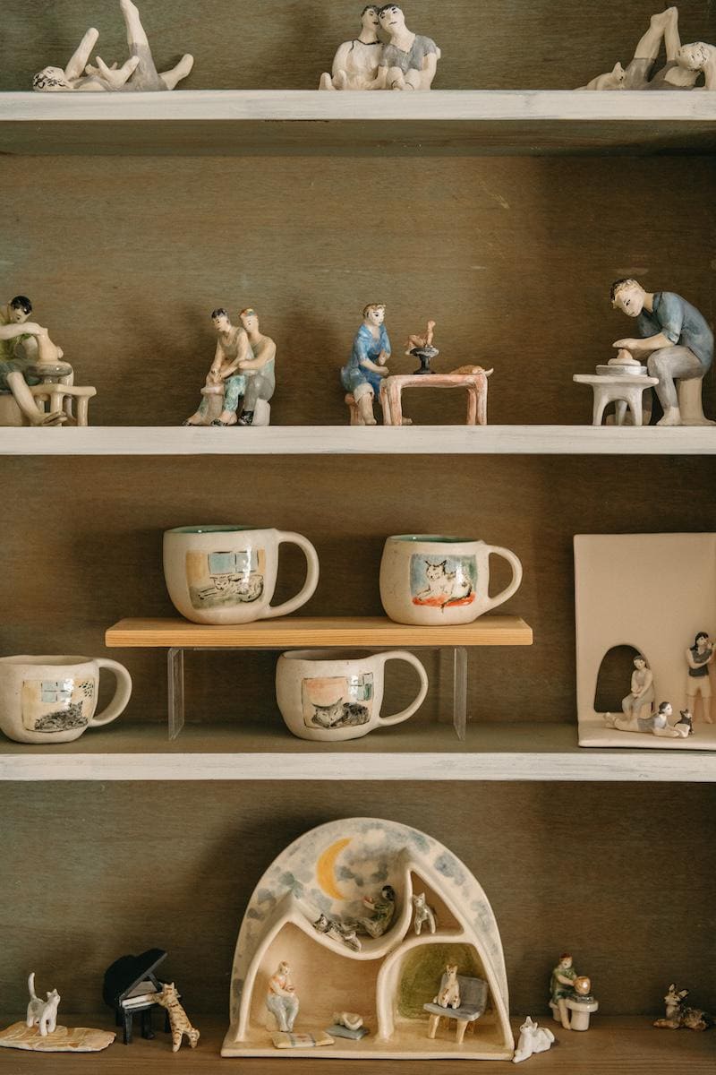 Bookshelf filled with Winking Cat Clay's mini sculptures, dioramas, and painted cat mugs.