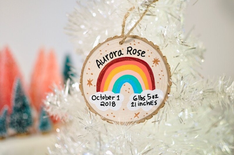 A hand-painted personalized holiday ornament with a name, birth date, birth weight and heigh, and a rainbow.