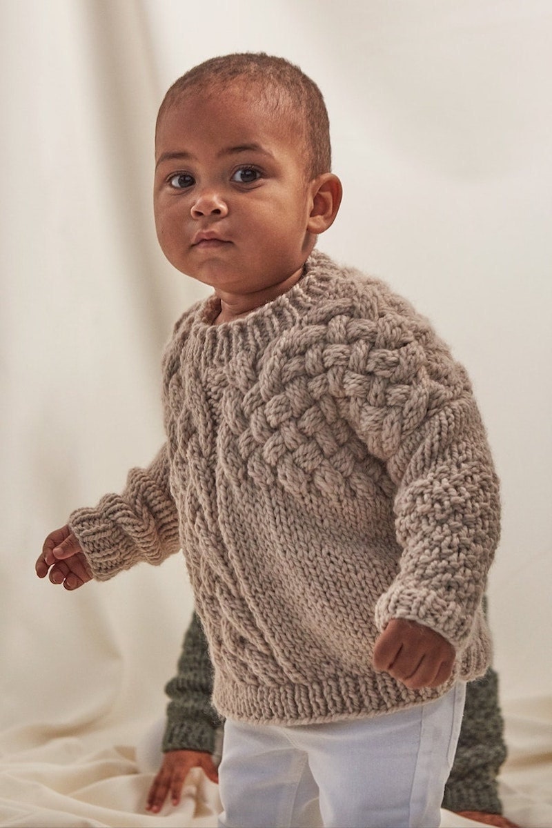 A baby wears a cozy oatmeal-colored chunky knit sweater