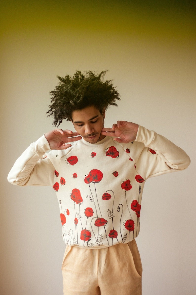 A Black man wearing a pullover sweatshirt featuring red poppy flowers.