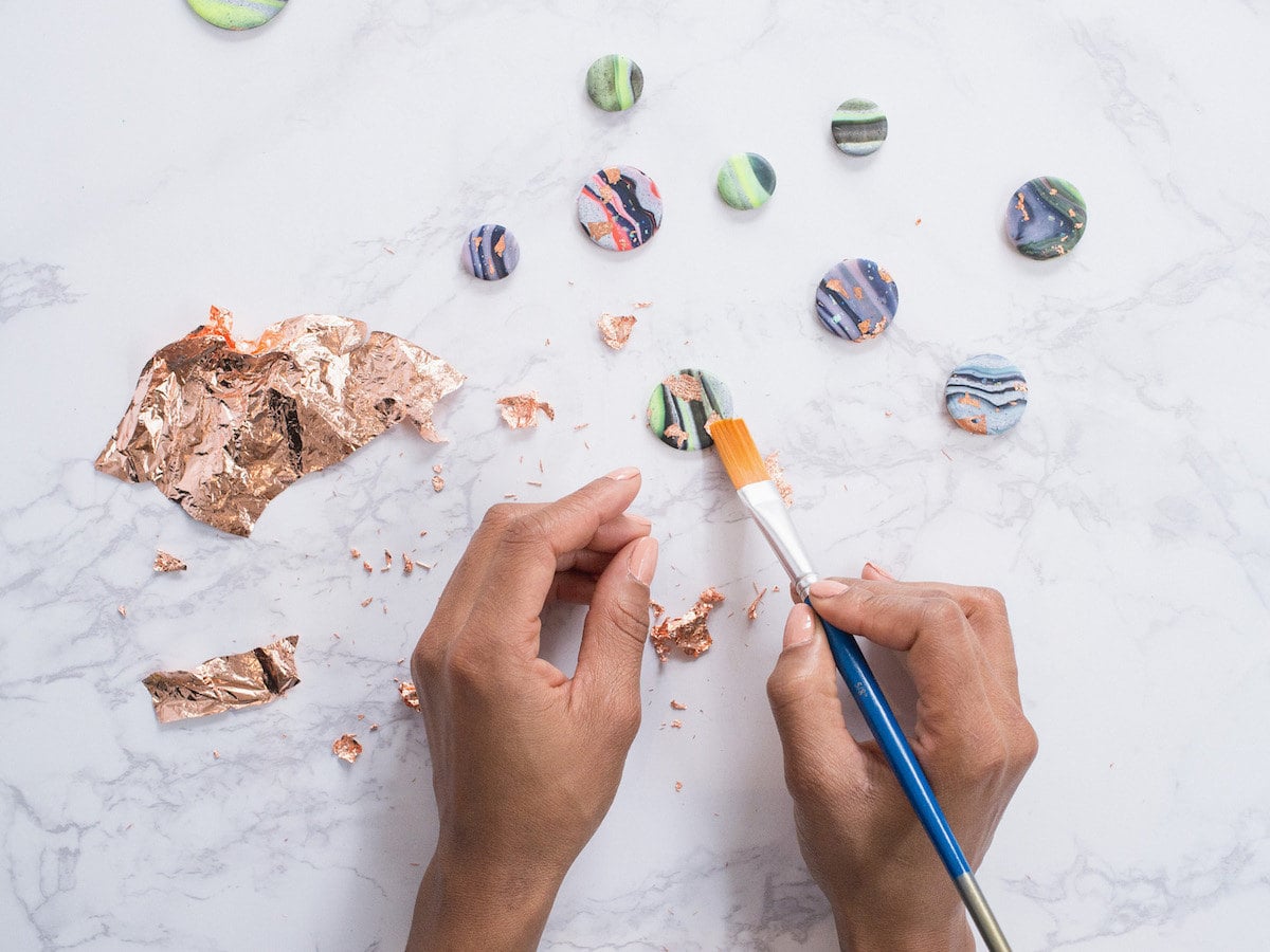 A woman adding gold leaf to handmade clay galaxy magnets. A woman adding gold leaf to handmade clay galaxy magnets.