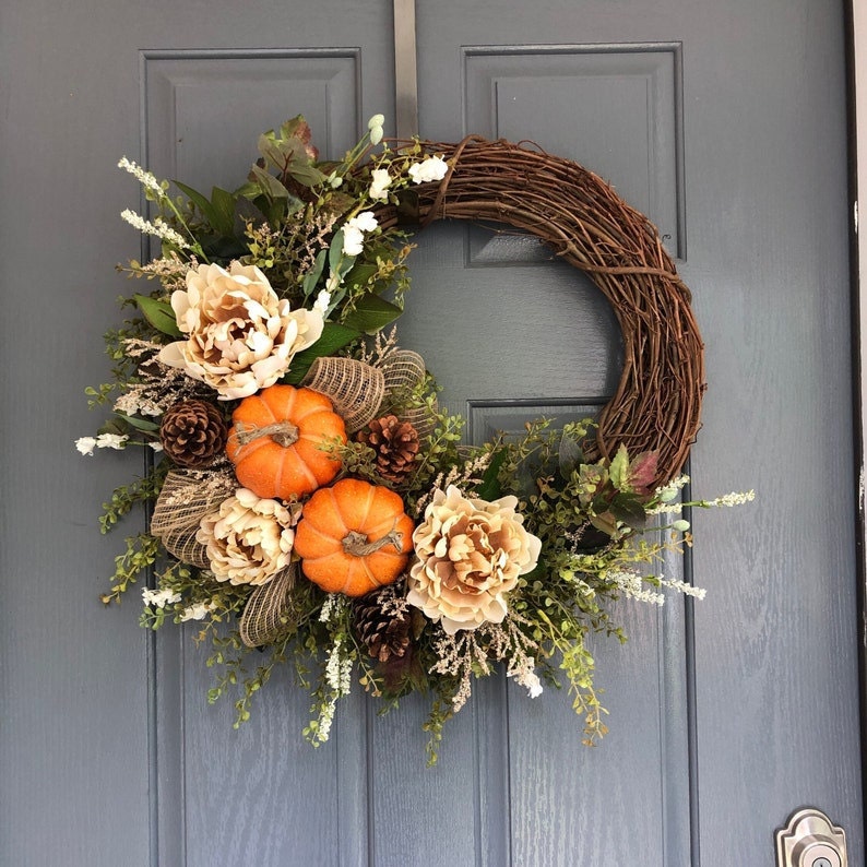 A fall wreath featuring pumpkins and cream-colored flowers.