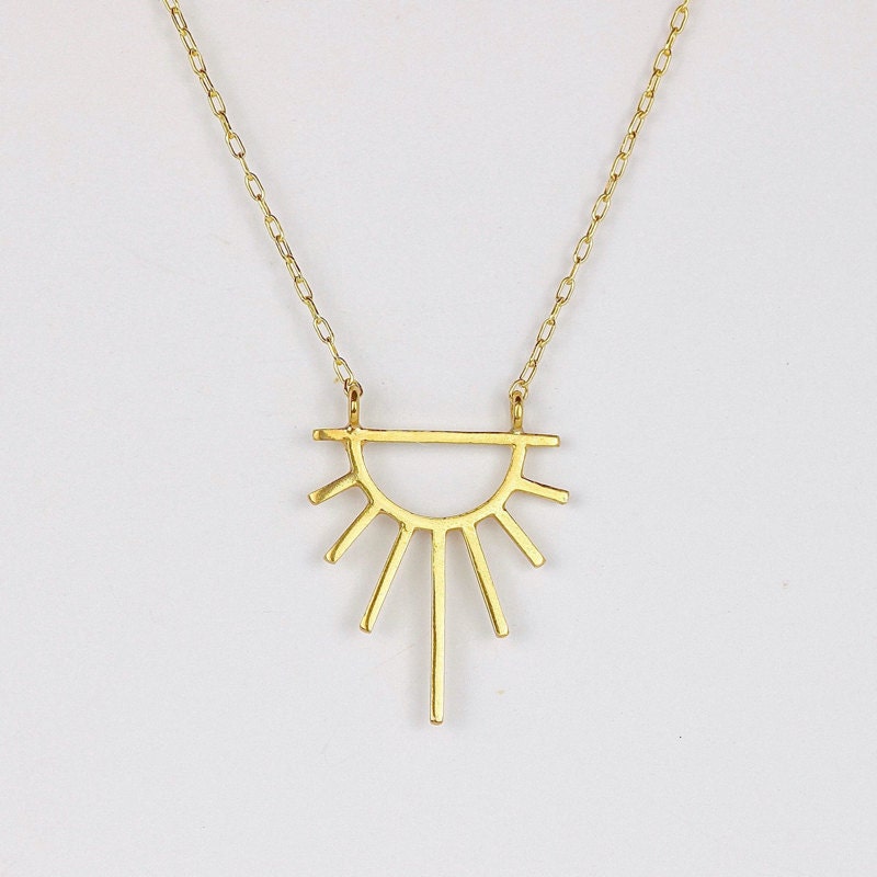 A golden sun necklace from Marcia Vidal Jewellery, a Black-owned shop on Etsy.