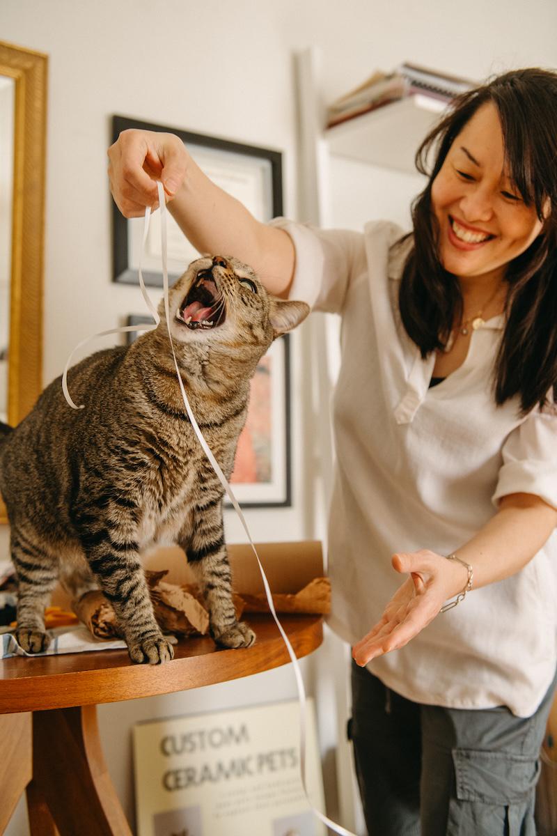 With a wide-open mouth, Nicky's cat plays with white ribbon atop her work table.