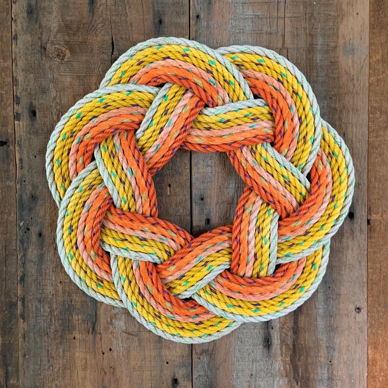 A had woven wreath made from reclaimed lobstering rope in bright fall colors against a dark wood background.