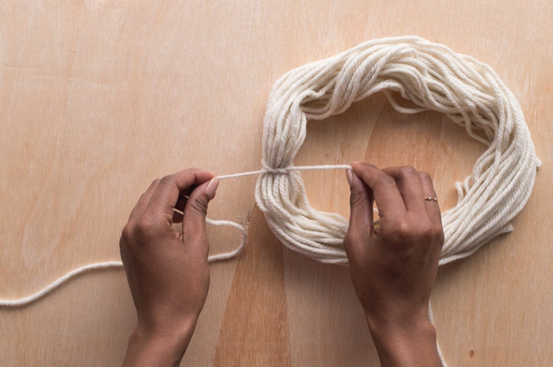Image of hands tying a knot around a yarn loop. Image of hands tying a knot around a yarn loop.