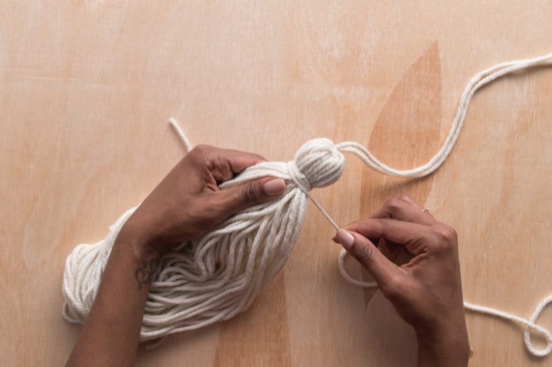 Image of hands wrapping a yarn loop to form a tassel. Image of hands wrapping a yarn loop to form a tassel.