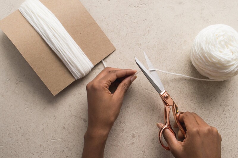 Hands cutting the yarn that's wrapped around the chipboard. Hands cutting the yarn that's wrapped around the chipboard.