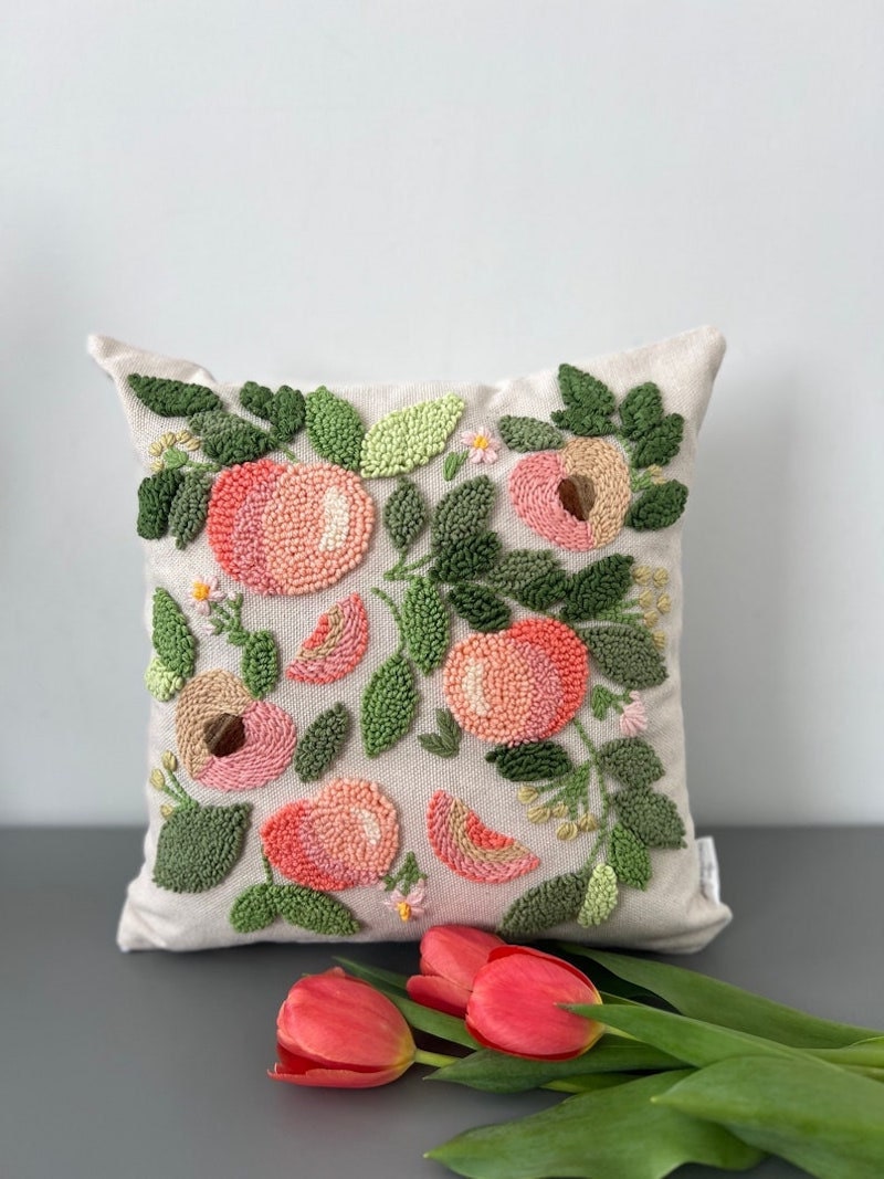 A couch throw pillow with embroidered peaches on it.