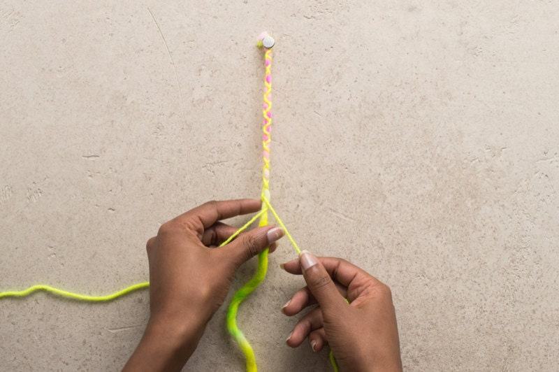 Hands braiding neon yarn.