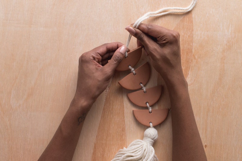 Image of hands tying a knot at the top of the finished wall hanging. Image of hands tying a knot at the top of the finished wall hanging.
