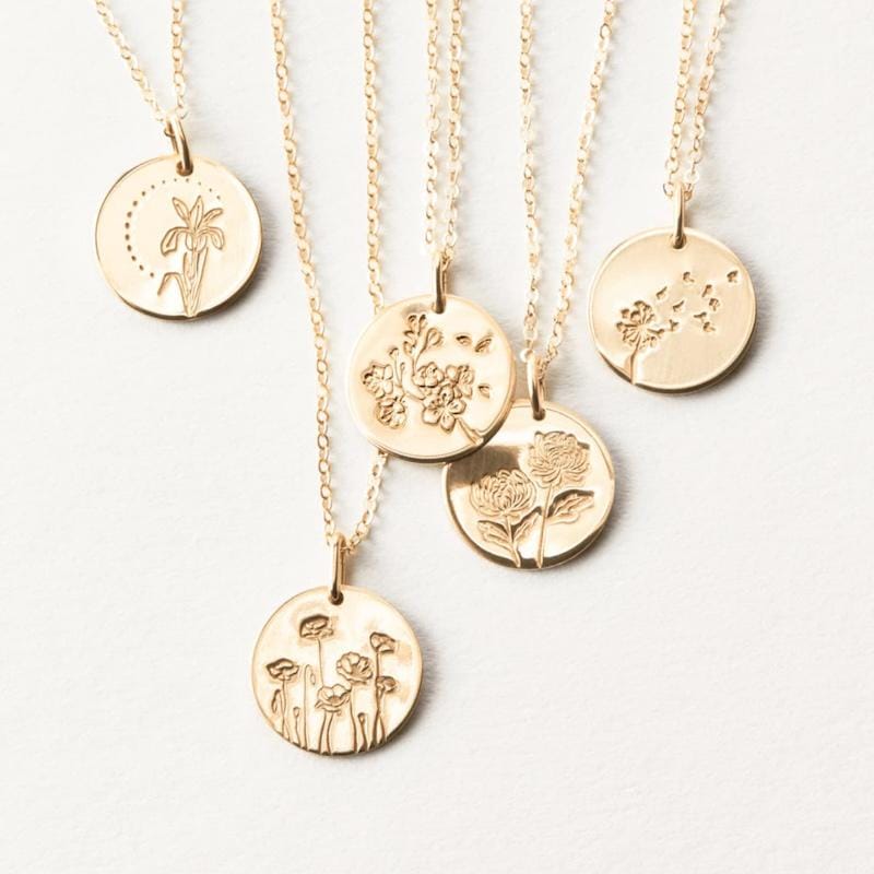 Five golden stamped birth flower pendant necklaces.