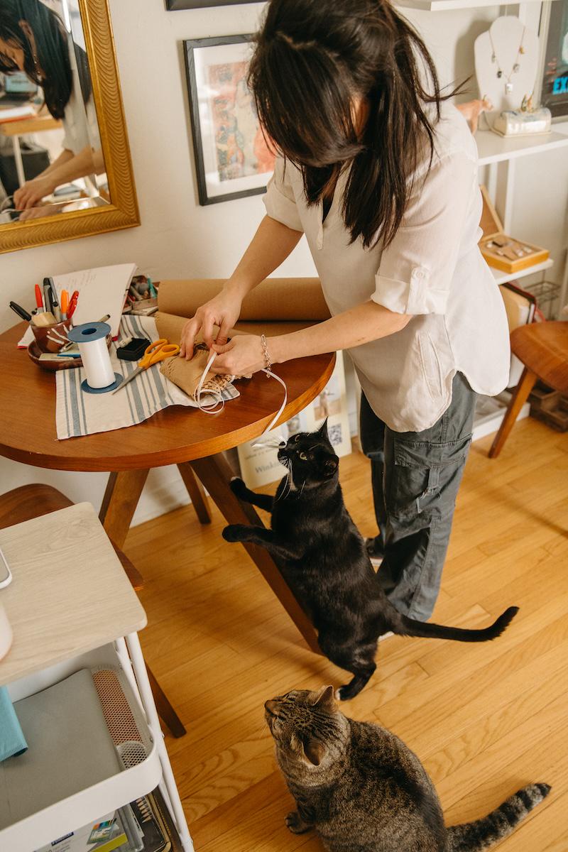 Nicky wrapping up an order while with her two pet cats supervise.