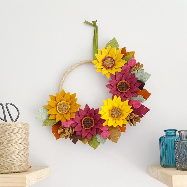 A fall wreath made out of felt sunflowers and leaves hanging on a wall.