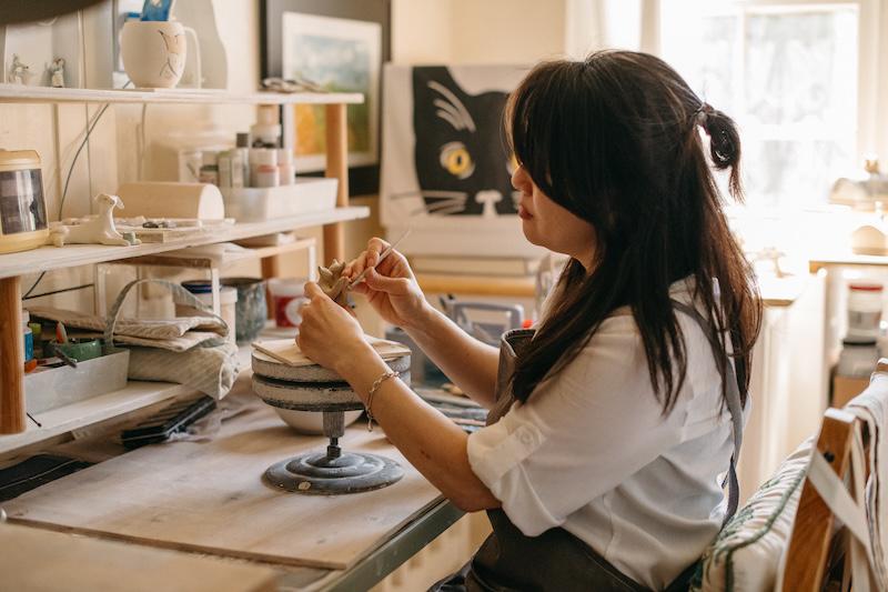 Nicky painting dancing cat figurines in her studio.