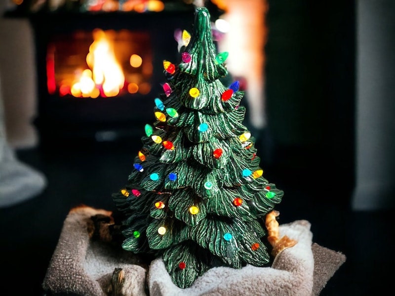 A green ceramic Christmas tree with lights with a lit fireplace in the background.