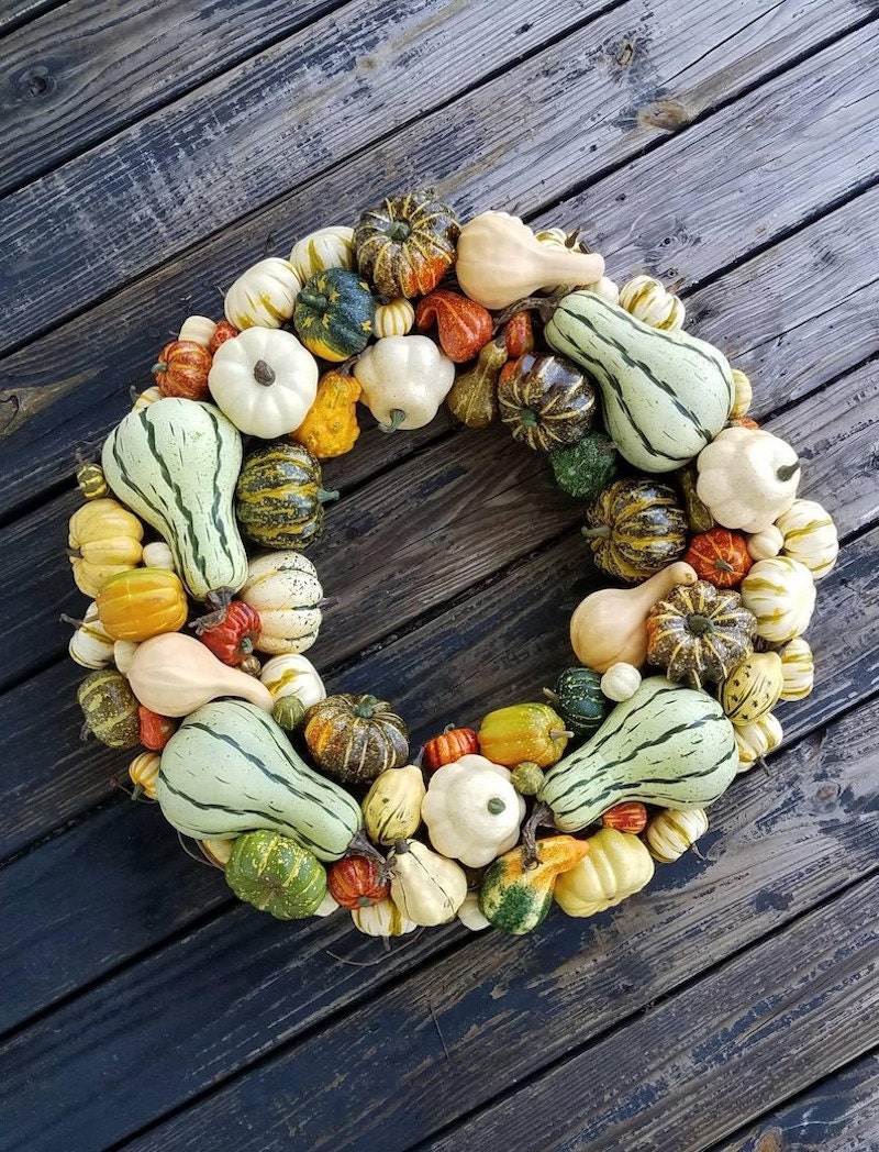 A fall wreath made up of different size pumpkins and squashes against a wooden background.