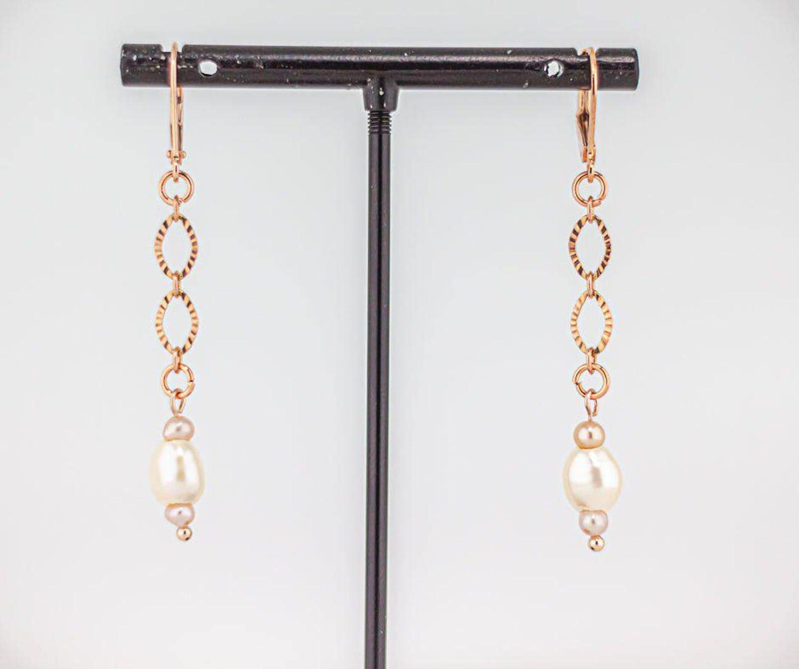 Dainty rose gold pearl drop earrings on a black jewelry stand