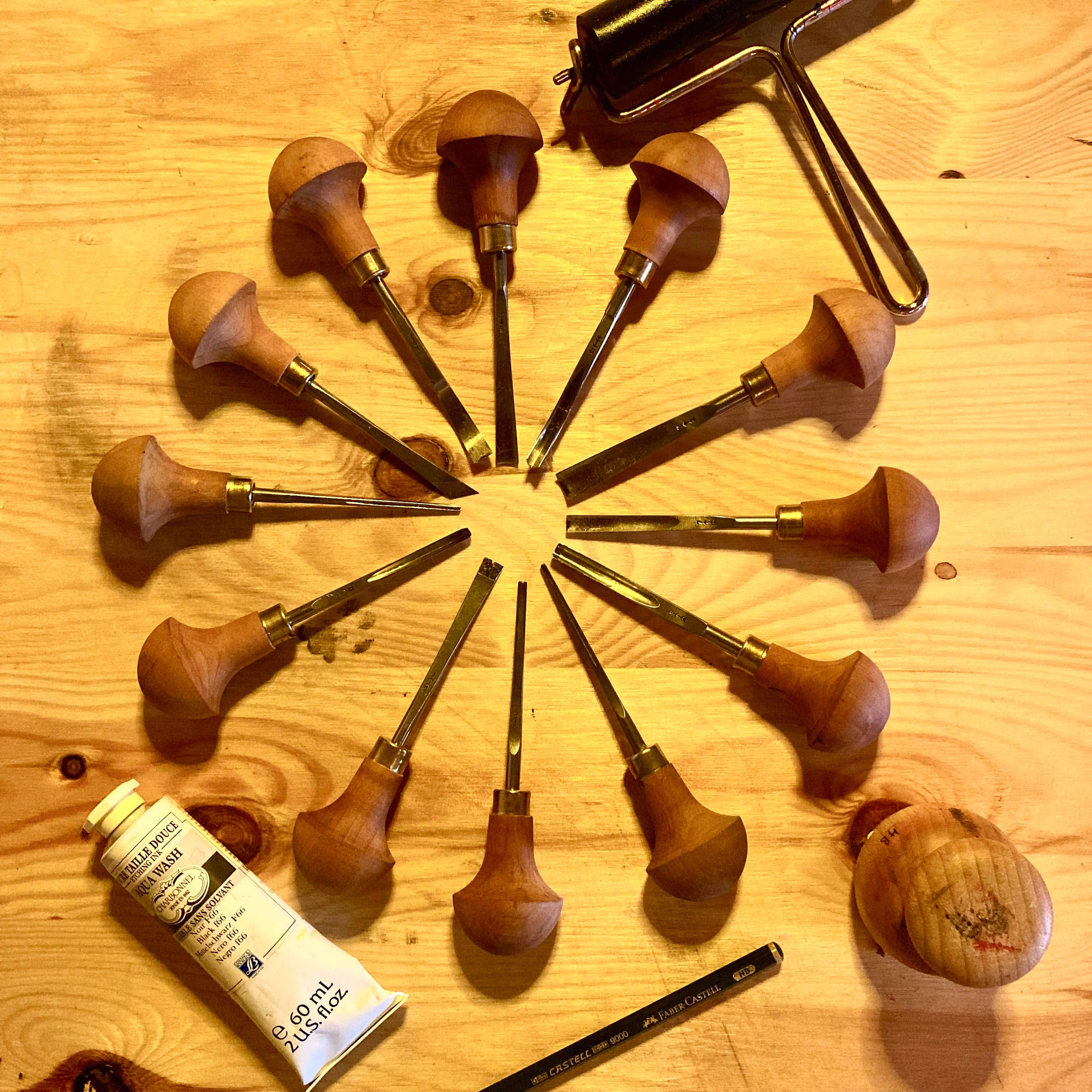 Outils pour la linogravure disposés esthétiquement, des gouges disposées en étoile, un tube d’encre noire à l’huile, un baren d’impression, un rouleau encreur et un crayon.