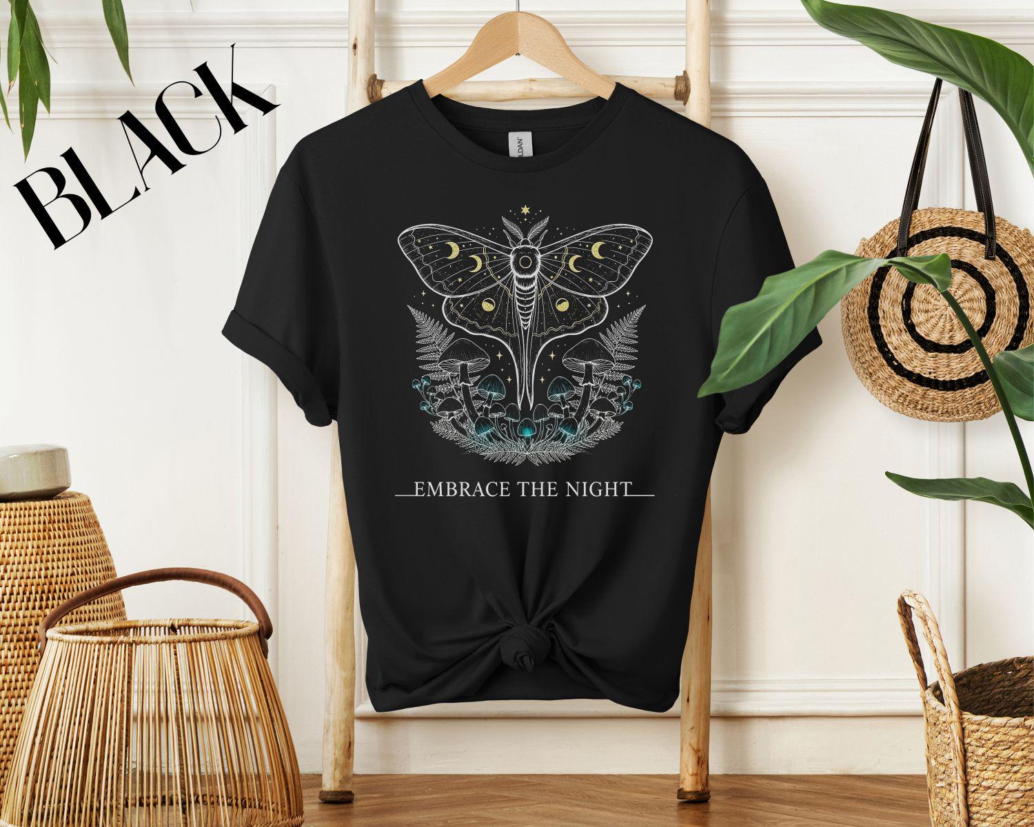 Celestial moth with moon phases above ferns and teal mushrooms; stars scattered; caption ‘EMBRACE THE NIGHT’ on black background.