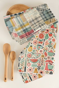 Colorful kitchen towells from KenmoreRd.Etsy.com. The colorful patchwork plaid dish-towel and retro mid-century kitchen design tea towel are on a white counter alongside wooden spoons and atop a wooden plate.