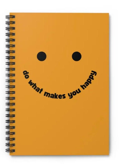 A bright orange notebook with a simple smiley face design and the text “do what makes you happy” written in bold black letters. The notebook has a black spiral binding.