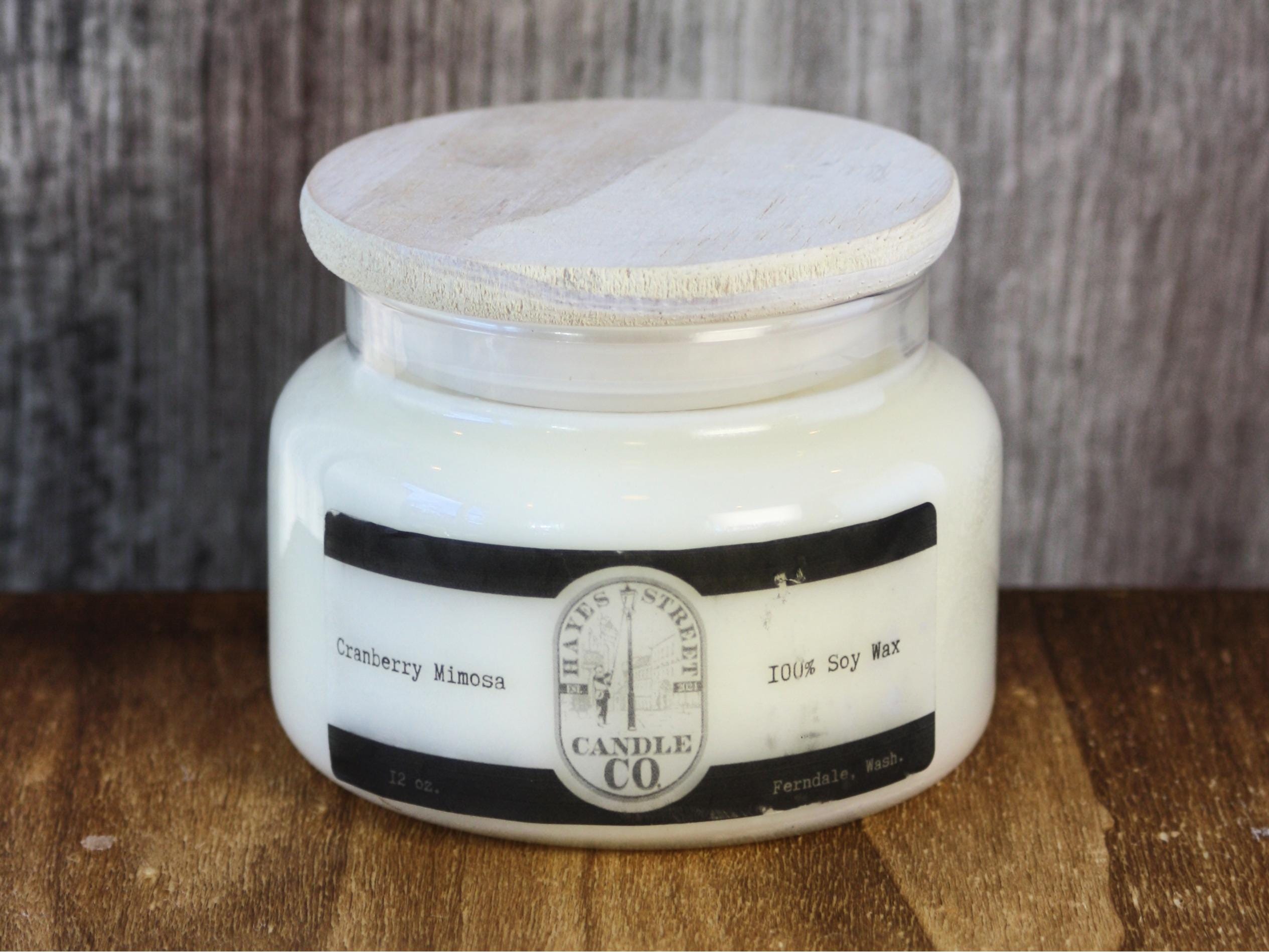 A very white-washed Cranberry Mimosa candle by Hayes Street Candle Company. The candle is in an apothecary style jar (which is tapered at the top). The candle comes with a white pine lid. Hayes Street Candle Company is based in Whatcom County near the Salish Sea and Puget Sound in Washington state. This is the West Coast of USA, specifically the Pacific Northwest. Each candle is made by Margie Creen. They are soy wax with no dye or additives. The apothecary style candles come with dual lead-free cotton wicks.
