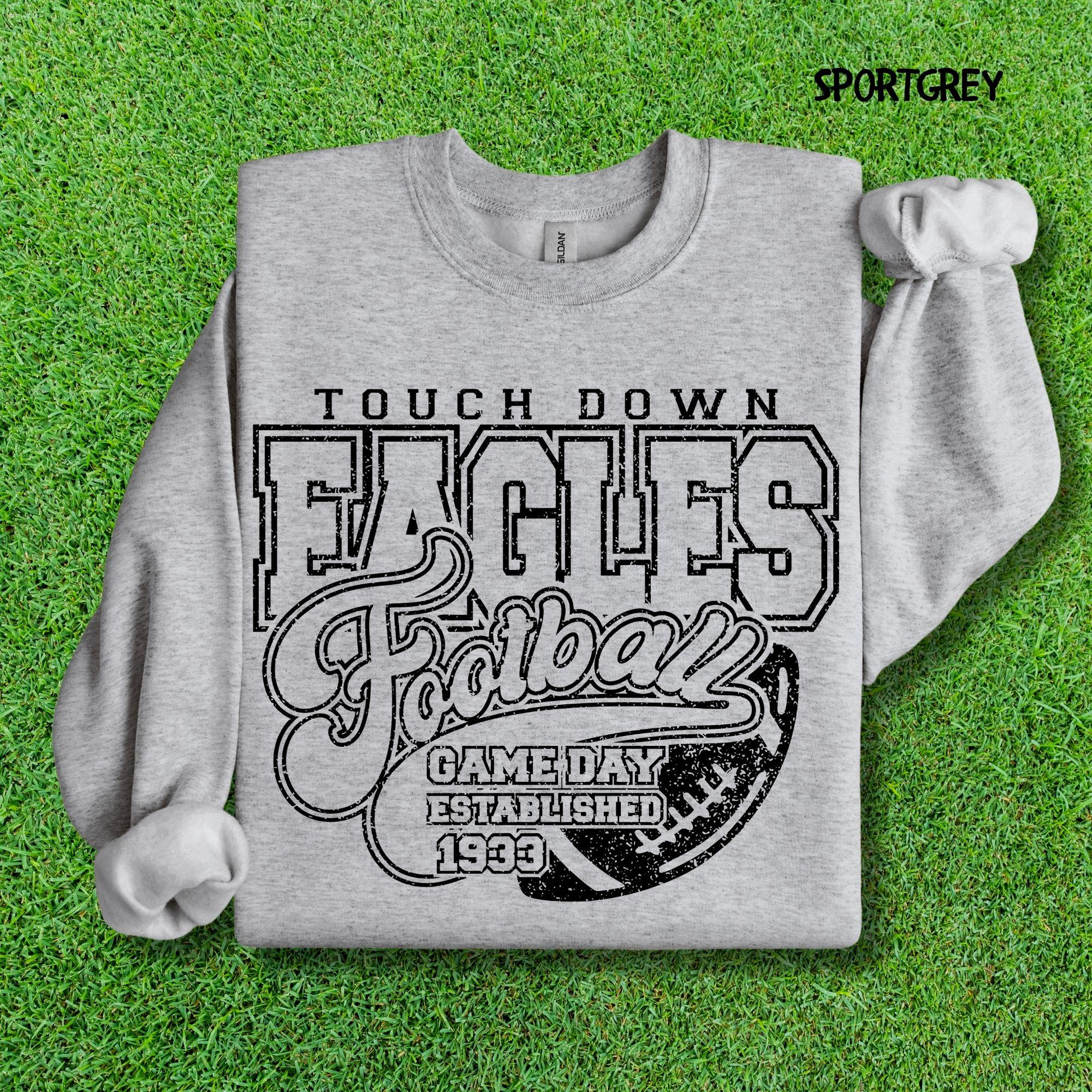 A vintage-style grey sweatshirt with Touch Down Eagles Football Game Day Established 1933 printed in a distressed black font, laid flat on a green grass background.