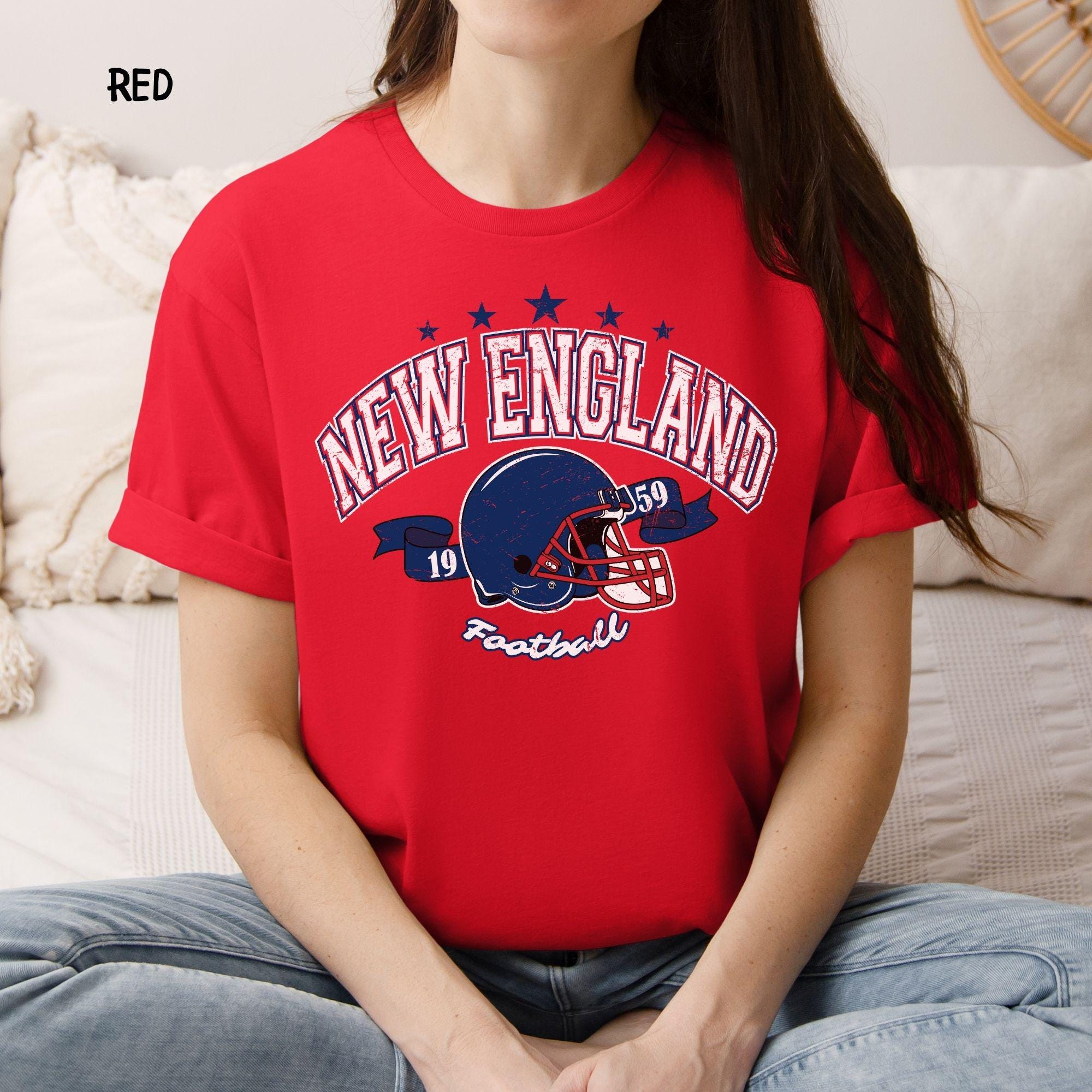 A person wearing a classic red t-shirt with a vintage New England Football helmet graphic.