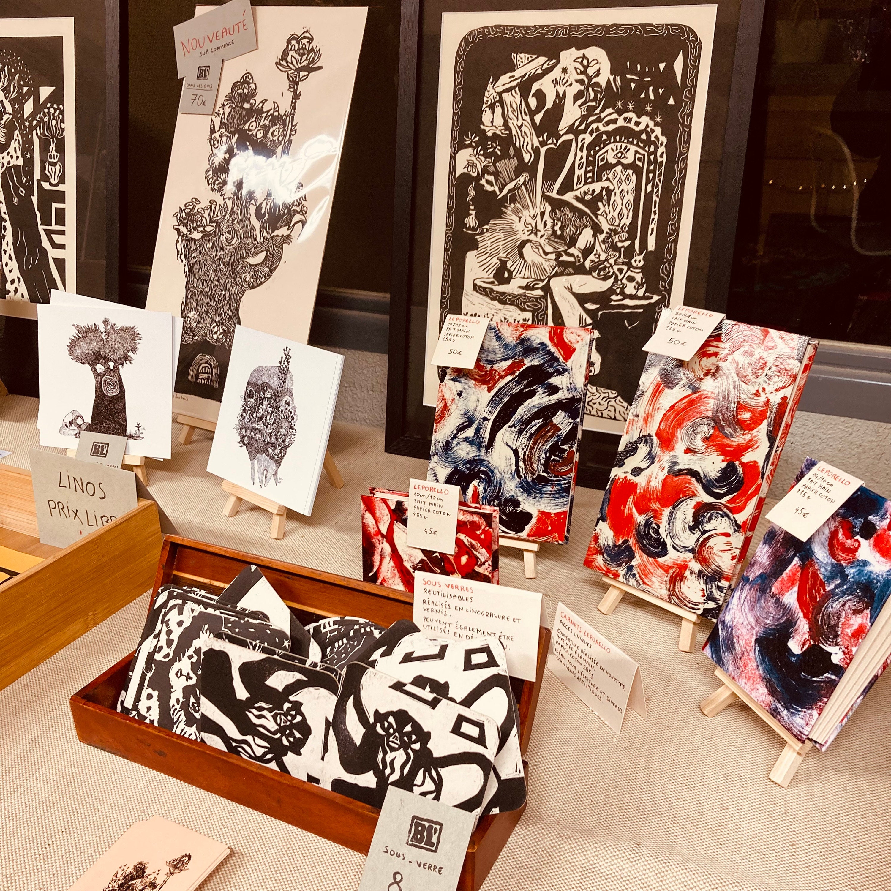Carnets colorés en monotype élégants, sous-verre en linogravure noir et blanc, présentés sur des mini chevalets. Créations artisanale en vente pour noël à Komuna.