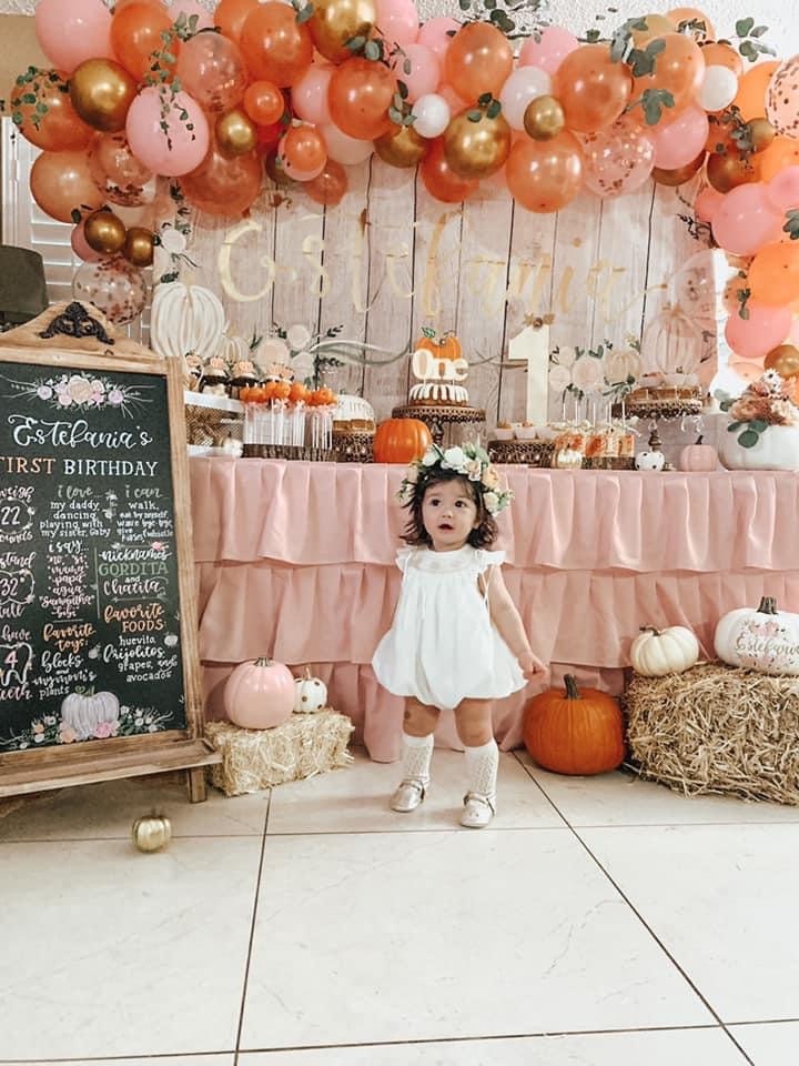 Baby on their first birthday surrounded by pumpkin themed backdrop