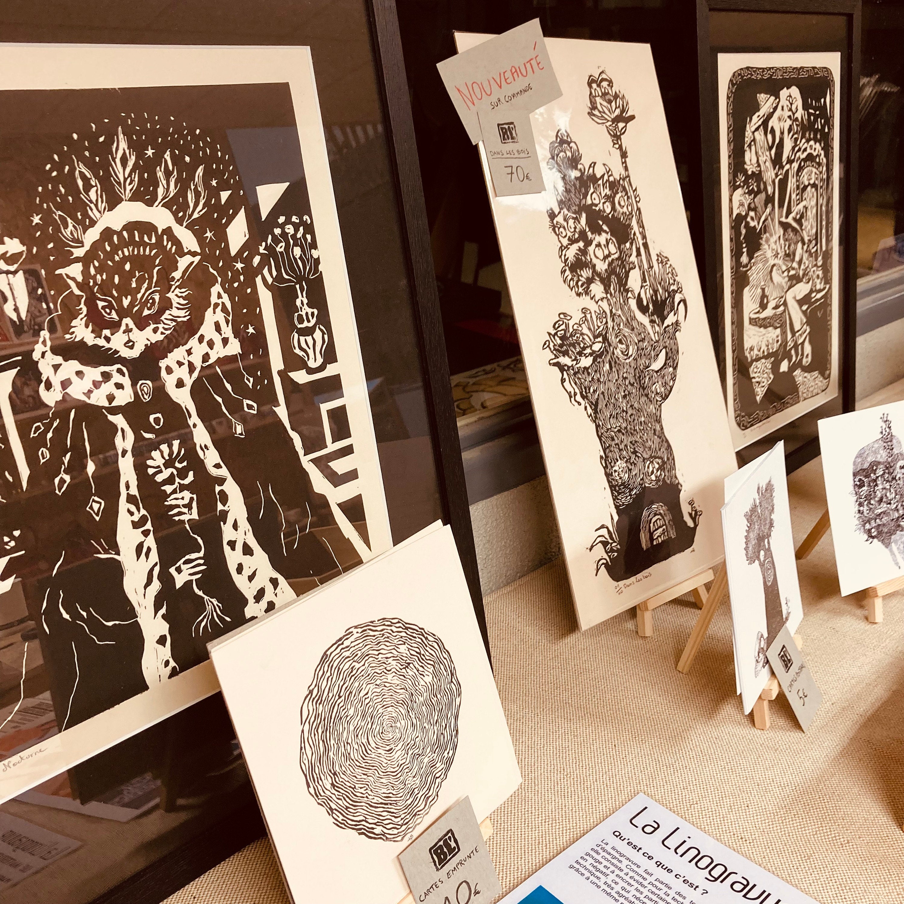 Stand d’exposition présentant des linogravures au format portrait noir et blanc encadrées, cartes disposées sur des mini chevalets.