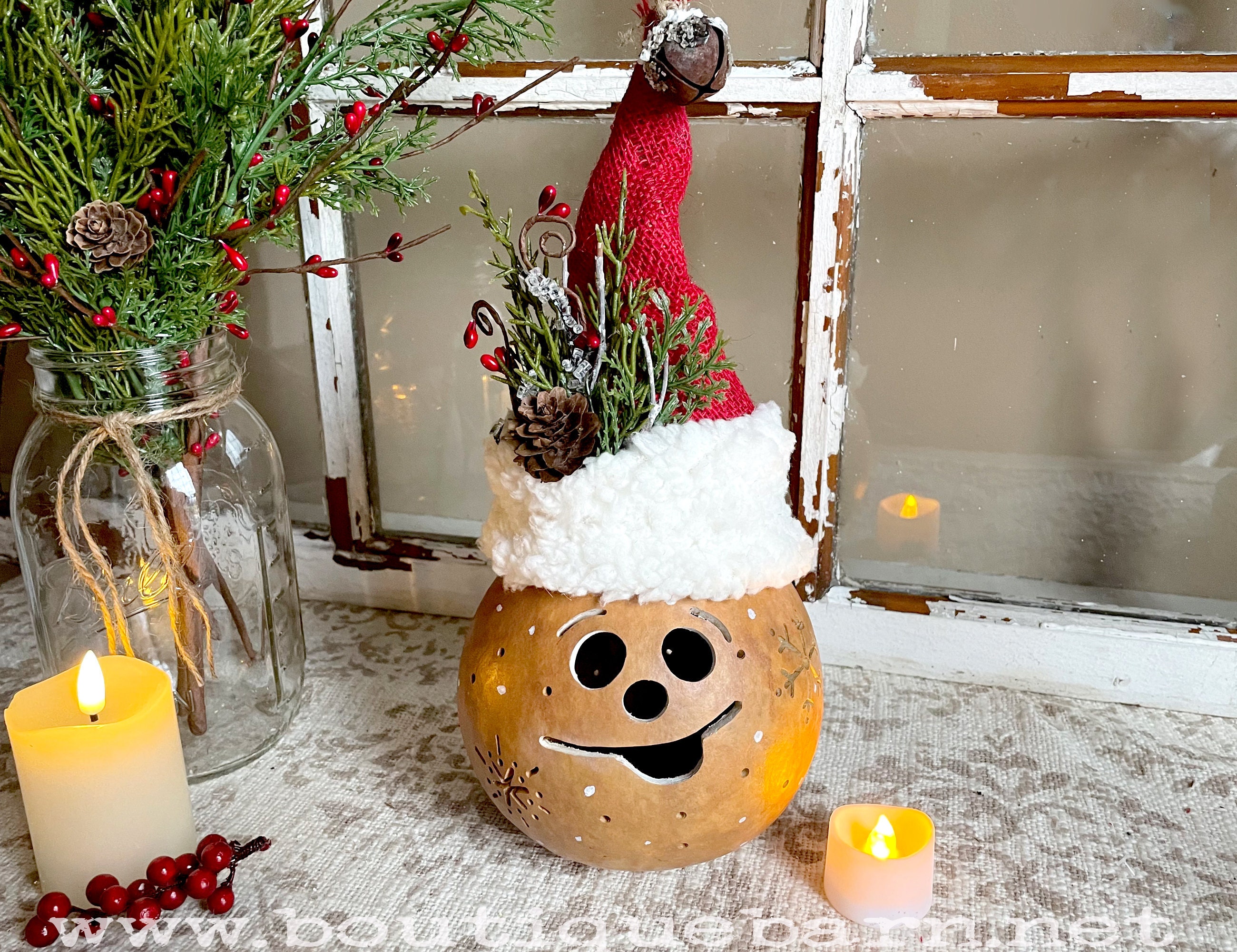 A handmade Christmas elf decoration. Made with a real dried gourd. The Chrismas Santa had is handmade with red burlap, faux fur trim and a rusty jingle bell. A battery operated candle lights up the gourd.