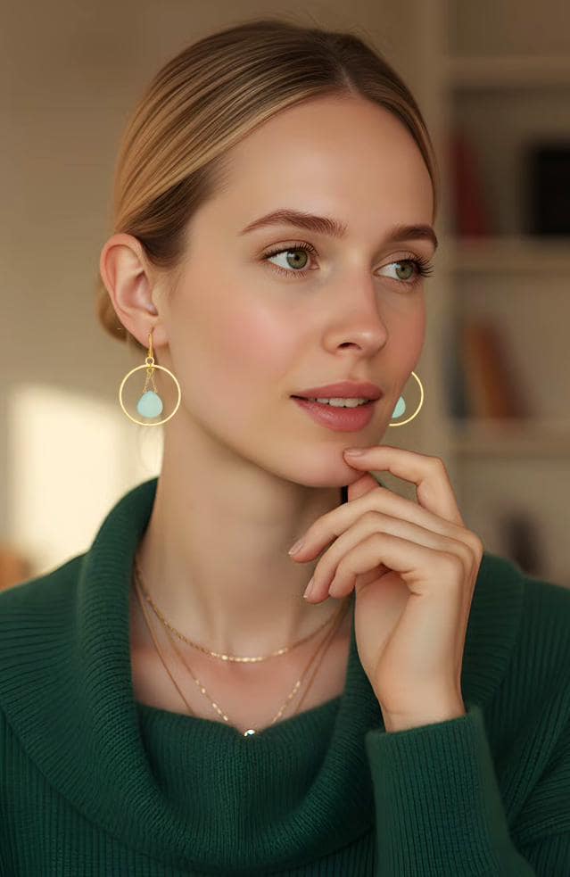 Woman in green sweater wearing big gold statement hoops with blue chalcedony gemstones.