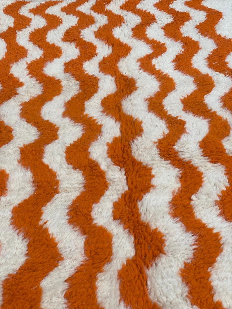 Handwoven Moroccan-style rug with orange and cream wavy stripes and knotted fringe