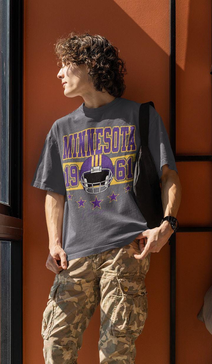 Gray crewneck worn outdoors featuring purple-and-gold Minnesota 1961 football helmet graphic—vintage varsity style