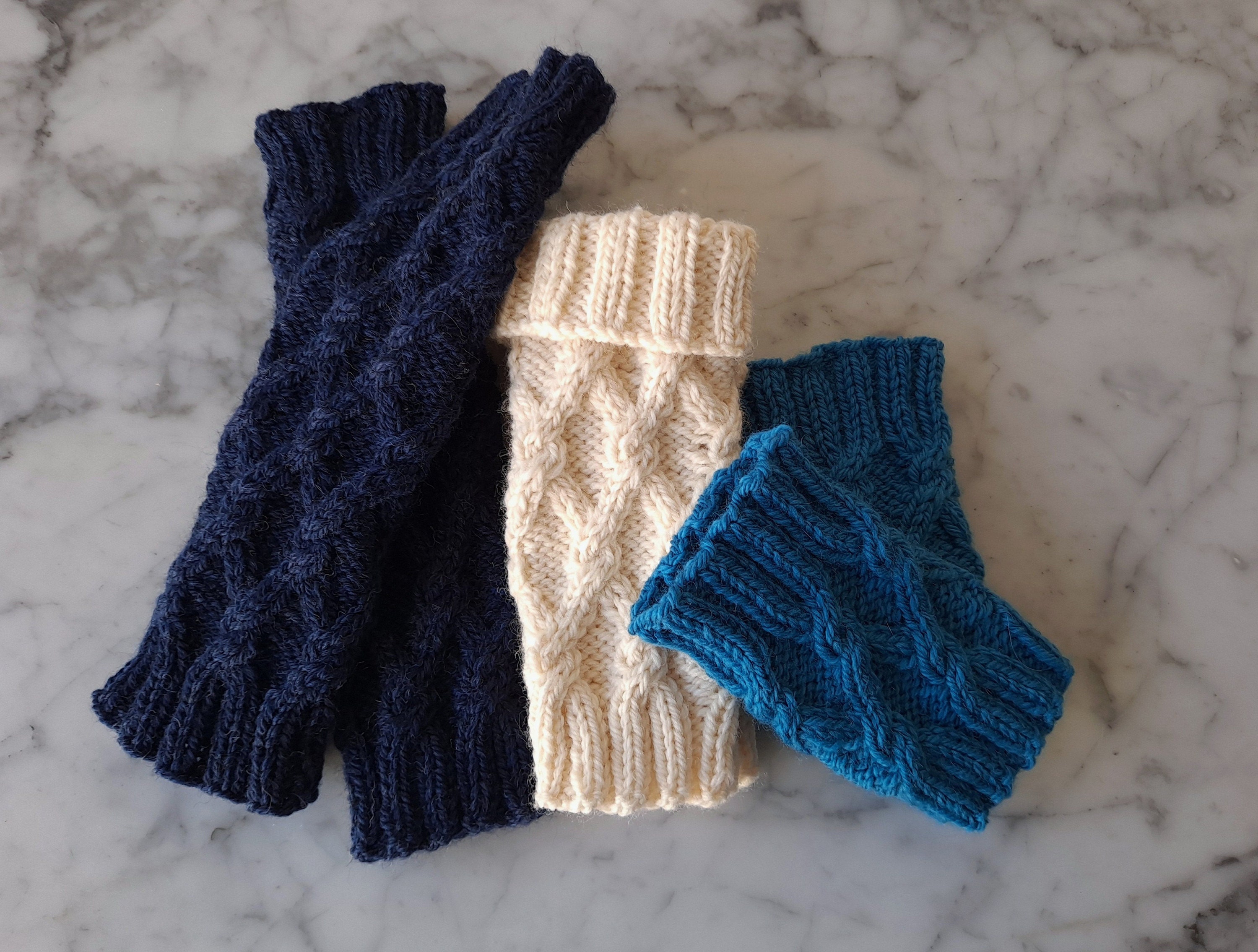 Three pairs of knittted wristwamers are displayed laid flat; the mittens are in different sizes and lengths.