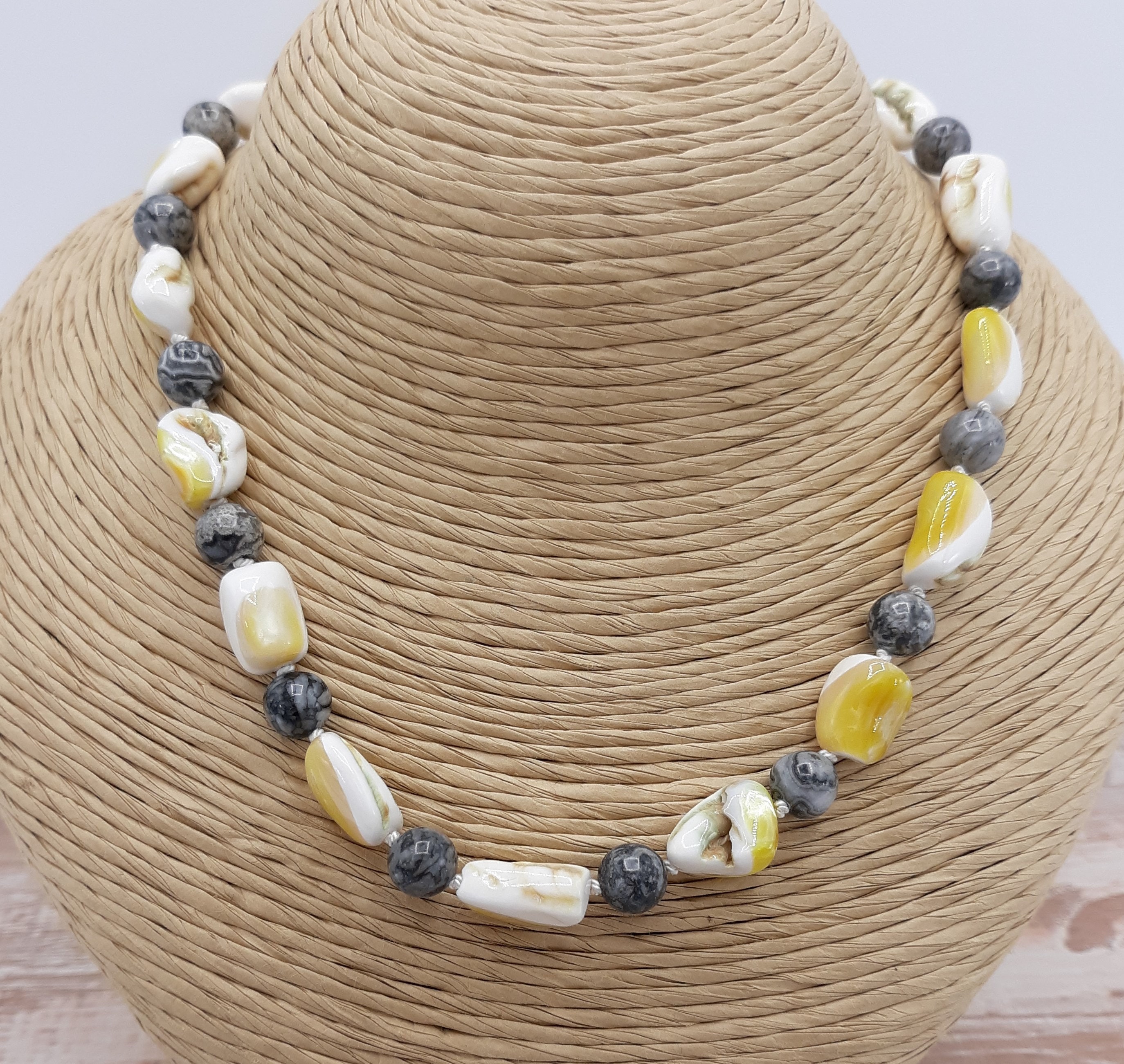 yellow and white shell alternating with gray and black crazy lace agate. Displayed on a twine bust.
