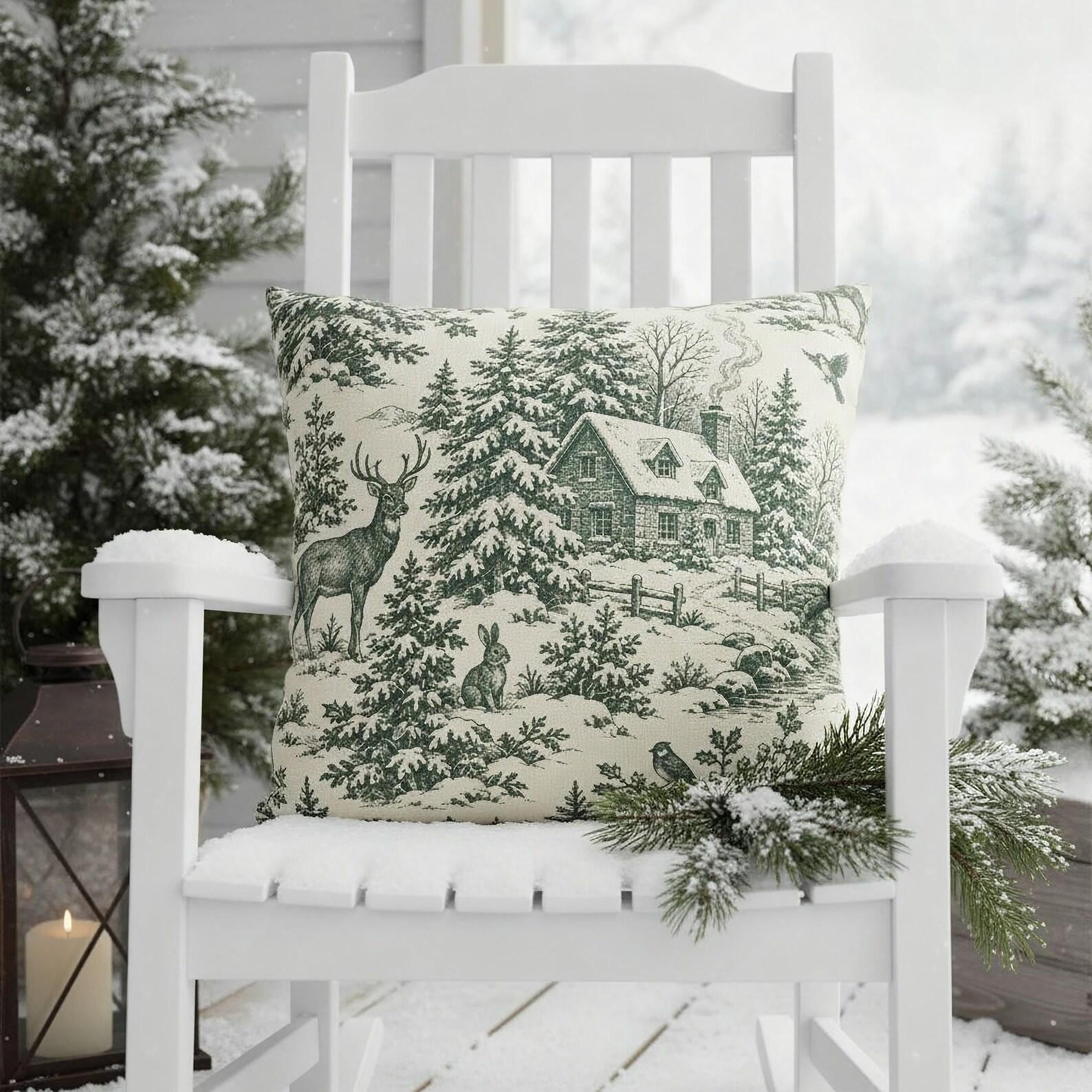 Green woodland deer and pine Christmas toile pillow on a white rocking chair on a snowy covered porch