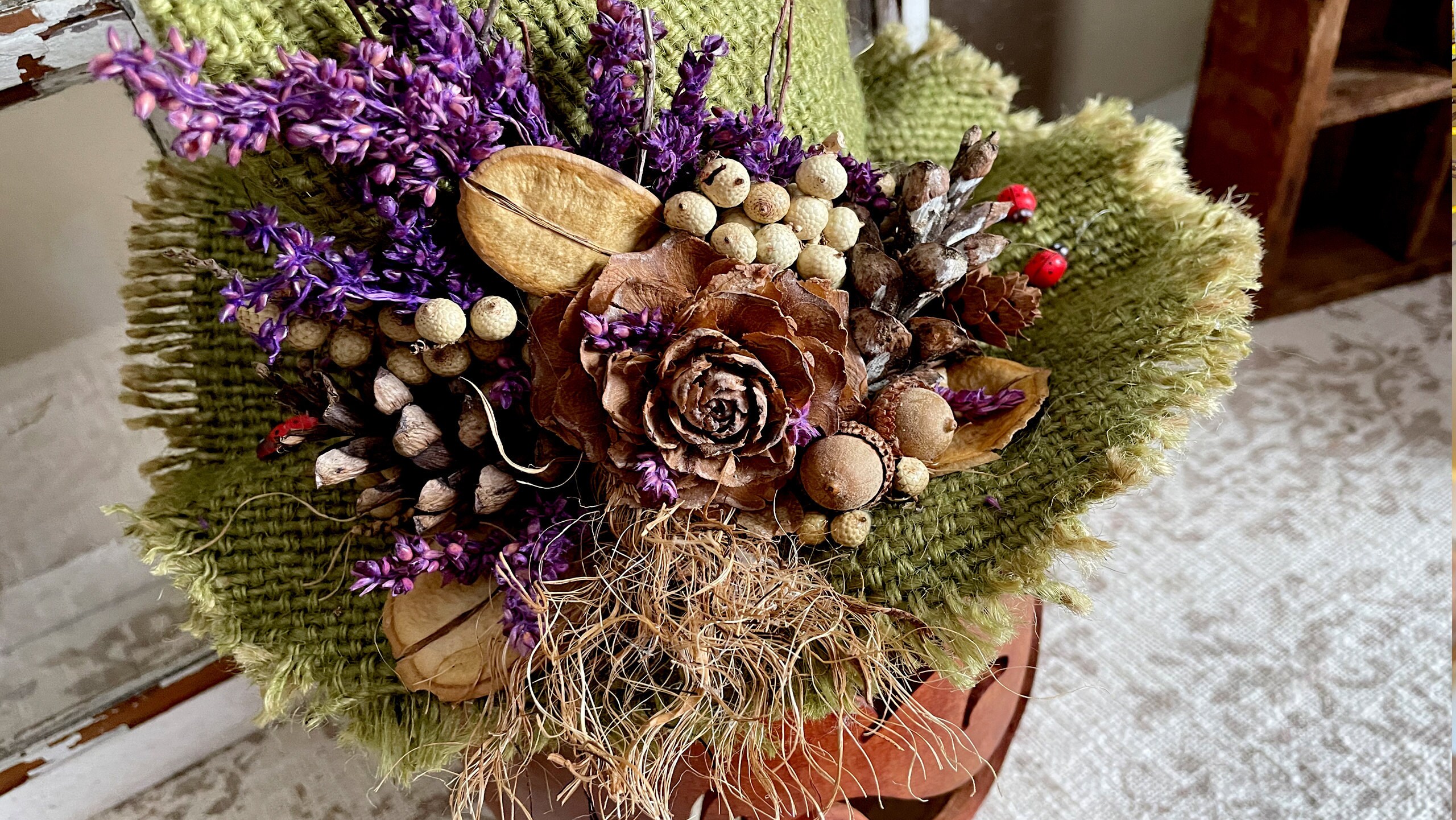 Image shows a close up of the botanical arrangement on top of Dew Drops hat. It includes lots of dried botanical berries and purple flower blossoms.