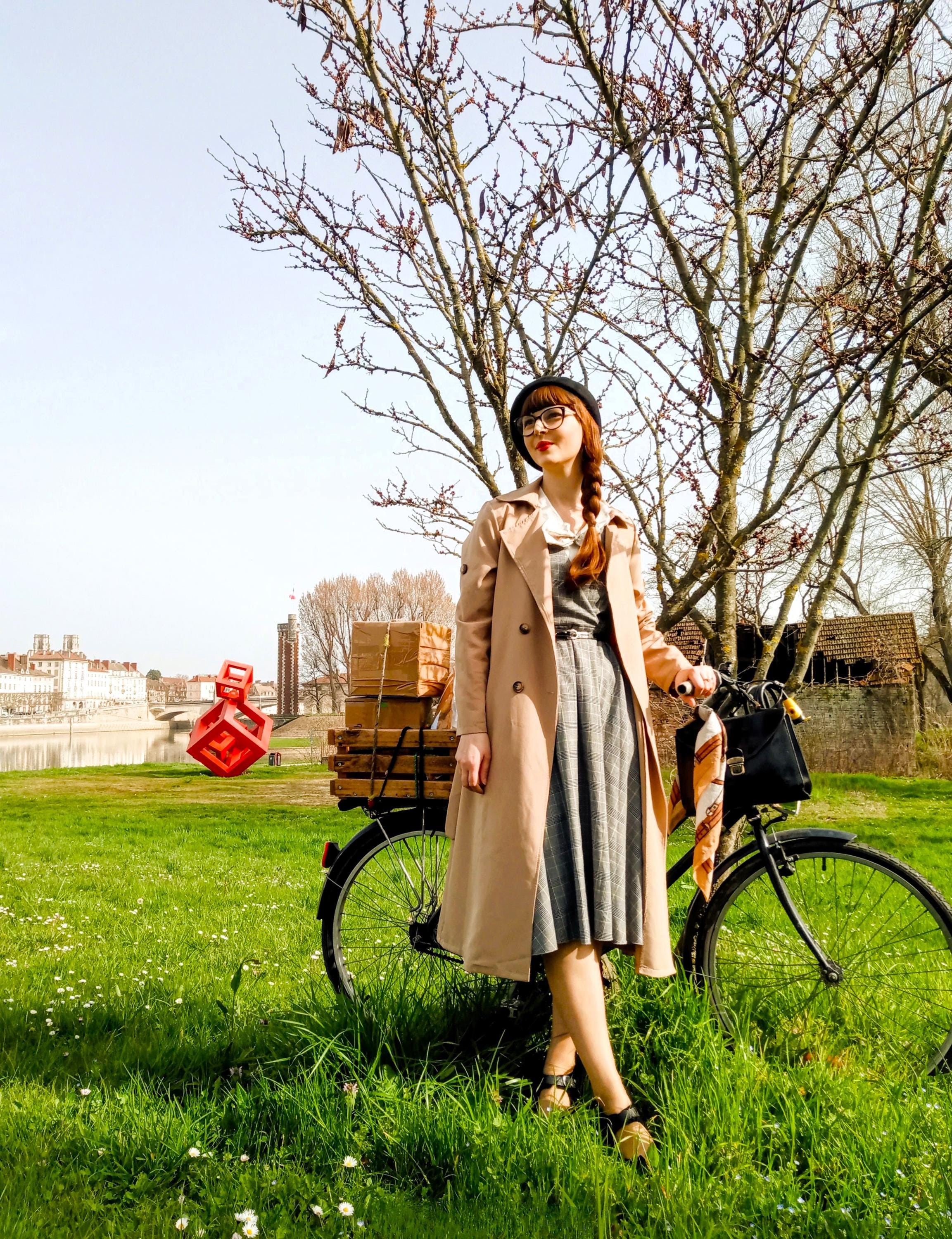 Vélo vintage de Laura Siméand (Un Style Rétro) garé sur la pelouse au bord de la Saône à Chalon-sur-Saône. Le porte-bagages est chargé de colis en kraft sécurisés dans une caisse en bois. En arrière-plan : vue panoramique sur la ville de Chalon, ses ponts et la cathédrale Saint-Vincent sous un ciel bleu.