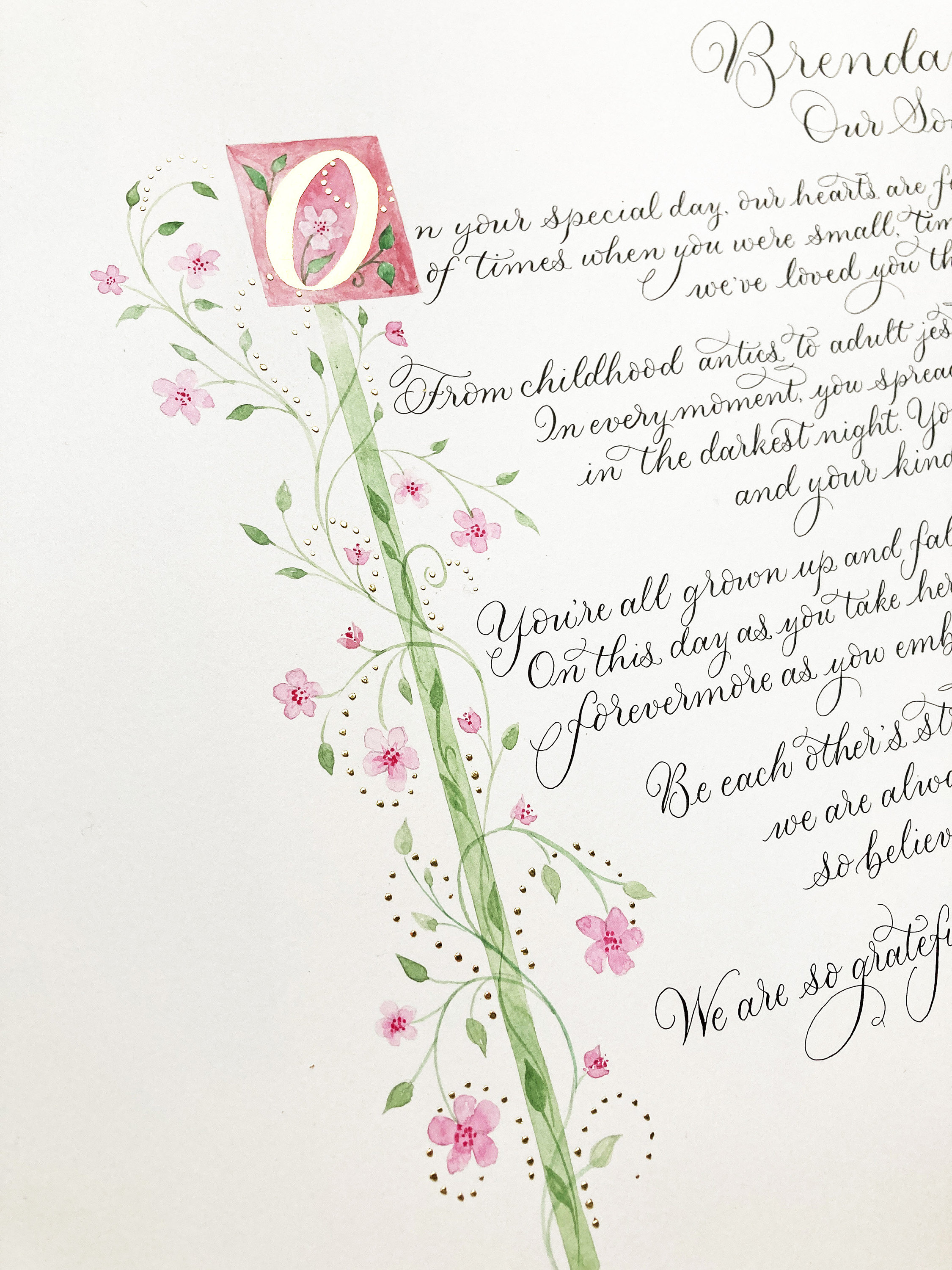 Close up of a calligraphy commission with decorative border illustrated in green and pink with flowers and gold leaf. By Claire Gould at By Moon and Tide Calligraphy, north west England