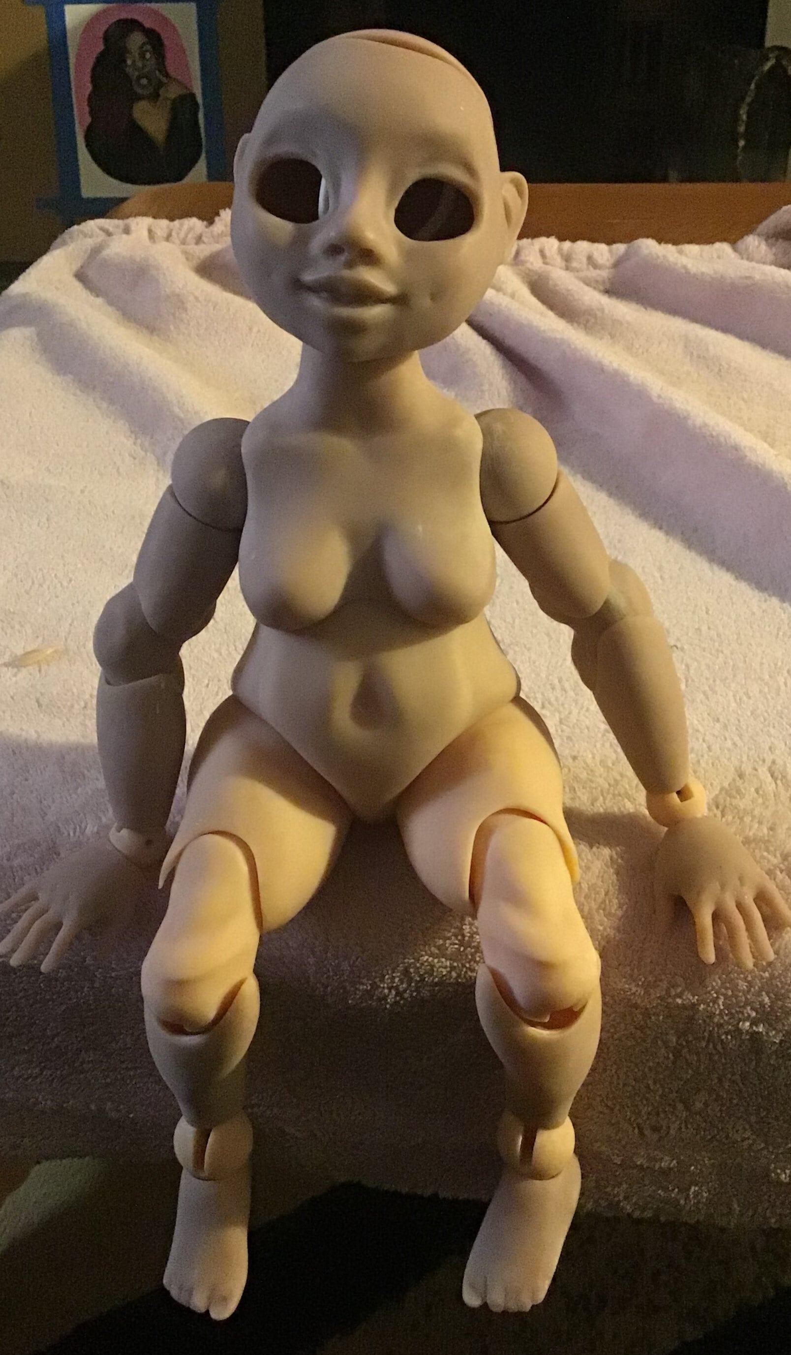 3D printed ball jointed doll in the color beige sitting in a table covered with a soft, pink, fluffy fabric.
