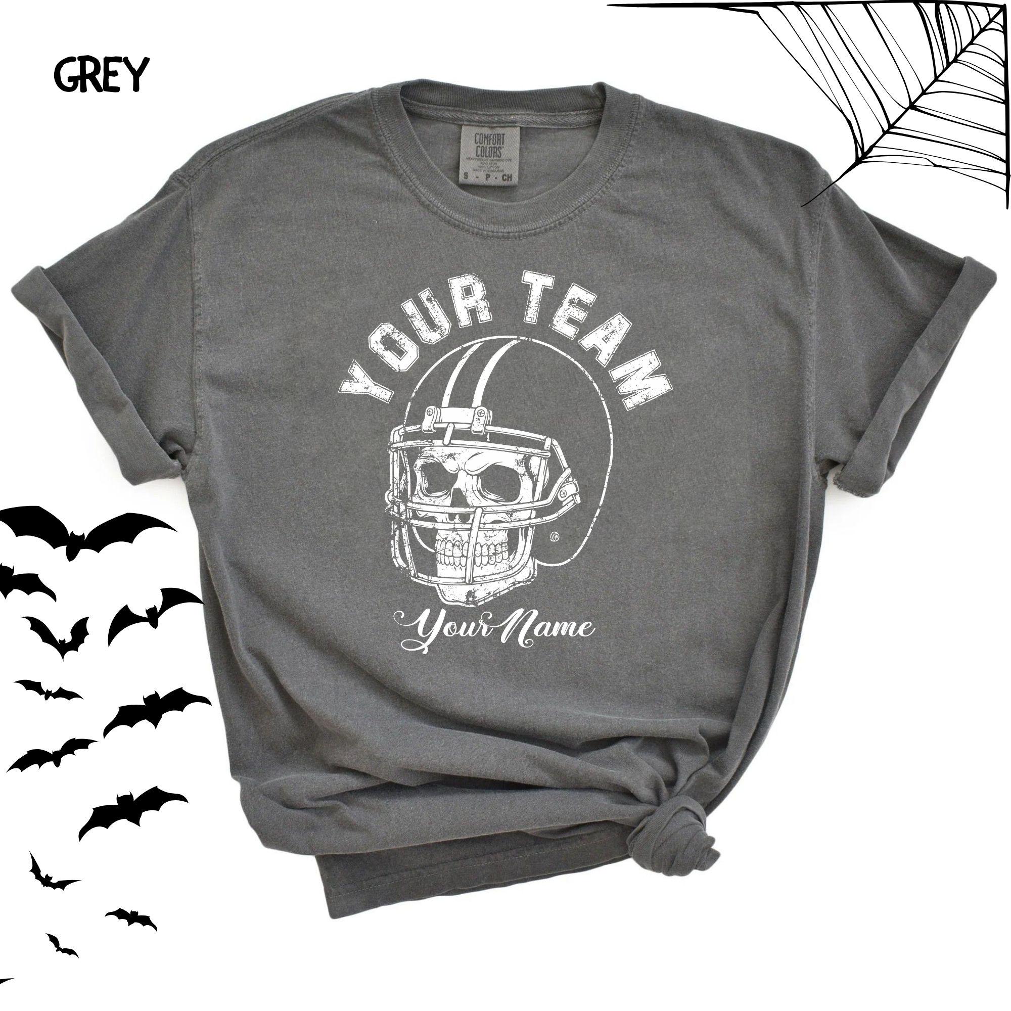 A person wearing a charcoal grey Comfort Colors t-shirt featuring a custom football design with a skull in a helmet.