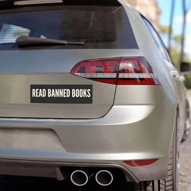 A silver car with a “Read Banned Books” bumper sticker affixed to the rear bumper. The sticker stands out with bold white text on a black background, promoting intellectual freedom and the right to read.