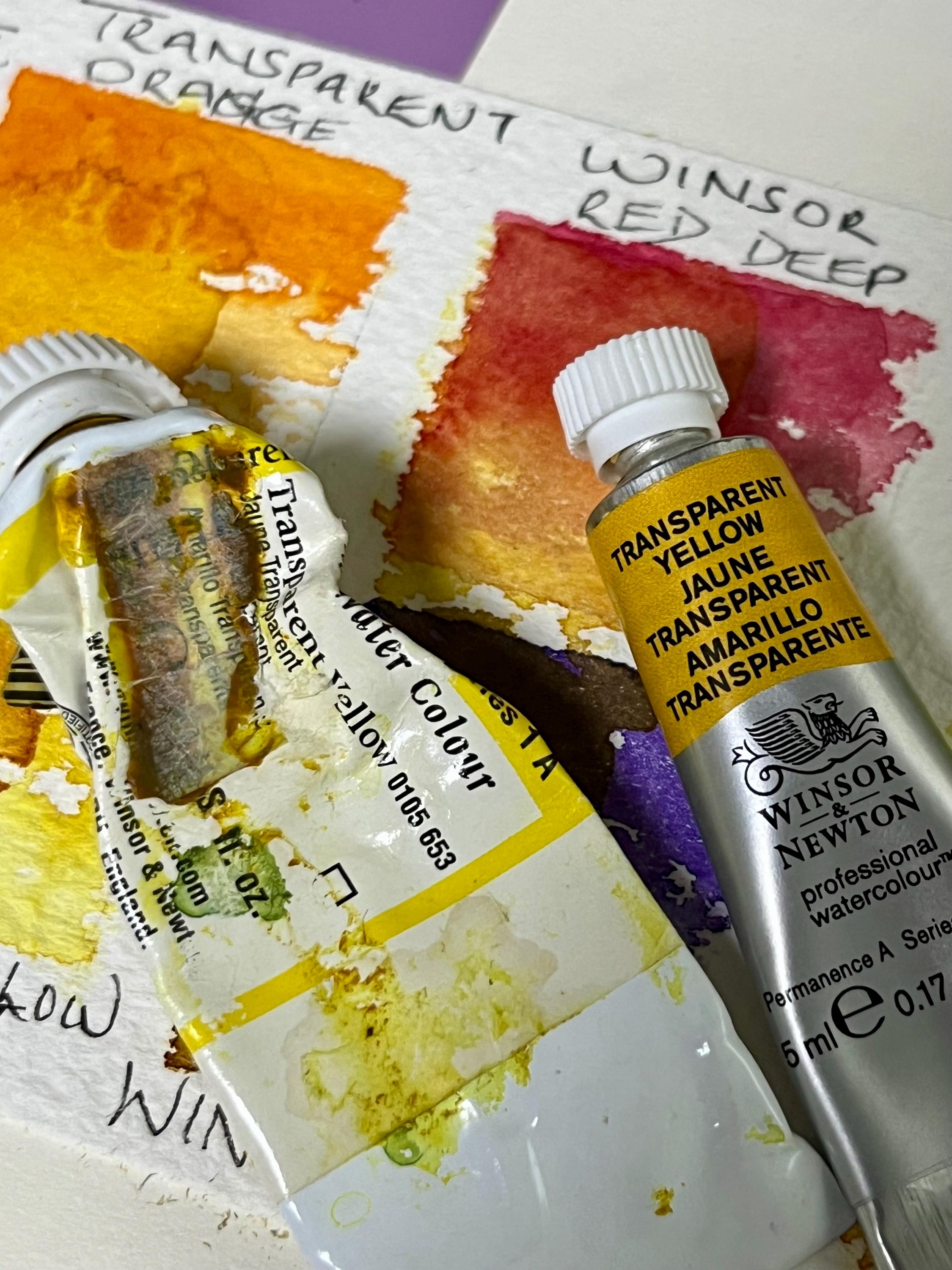 Two tubes of watercolour paints one new the other used up with a background of the colours on rough watercolour paper swatches.
