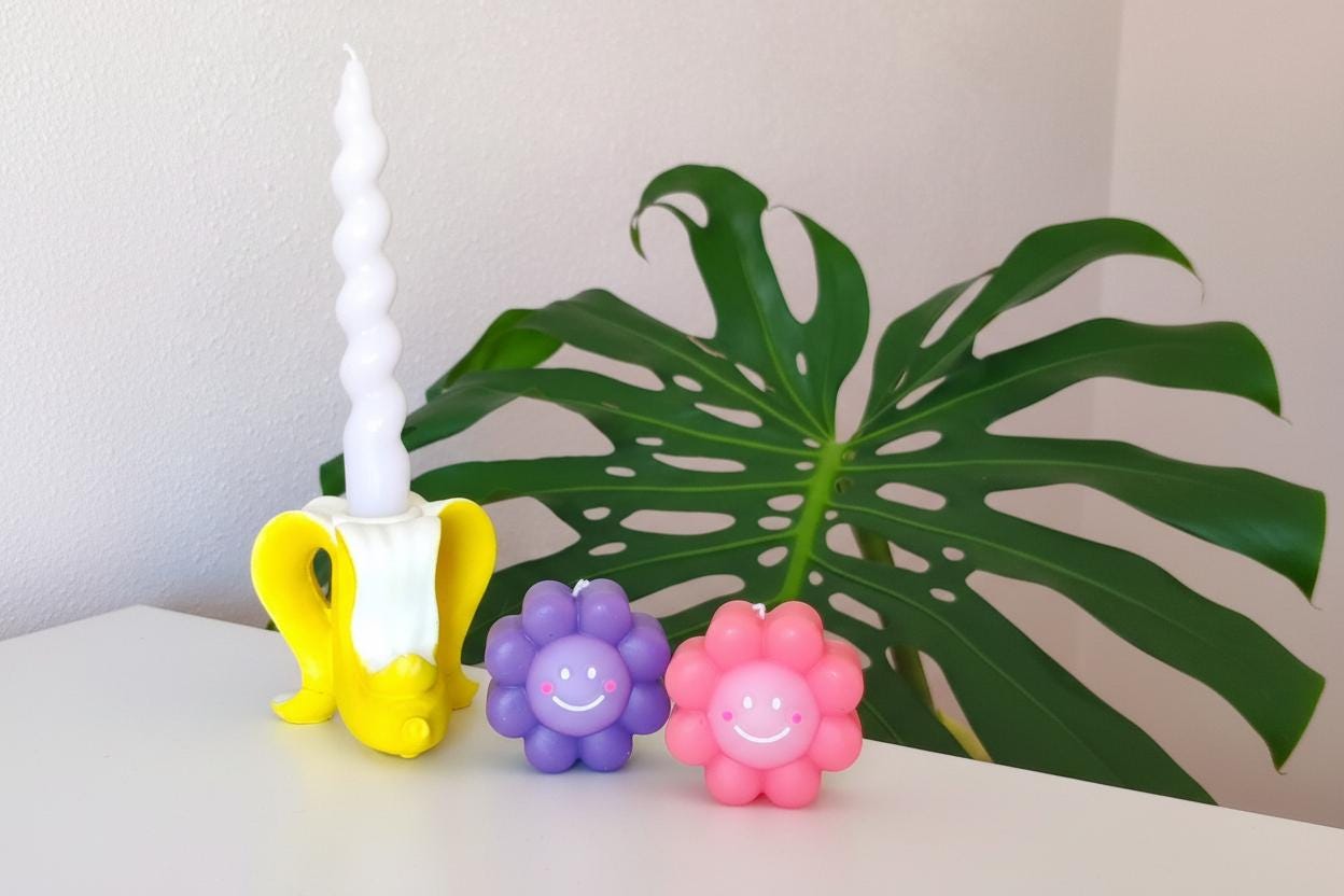 banana candle holder and flower candles in a table. monstera plant leaf behind.